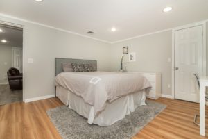 Picture of bed with gray bedspread and gray rug and hardwood floors 